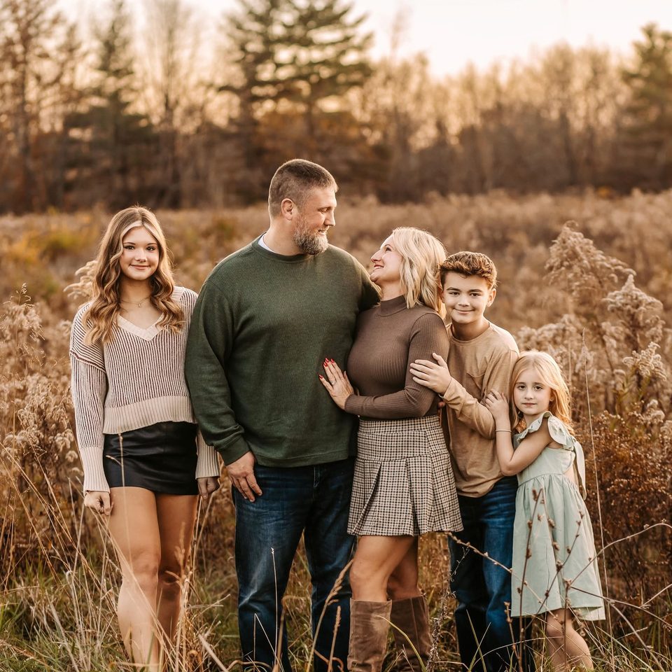 Addam Lewis and his wife, Anna, standing in a field of tall autumn grass with their three children.