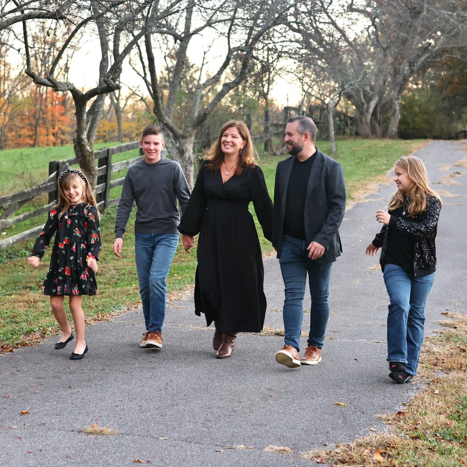 Christian Moore and his wife, Natalie, walking down a tree-lined path in autumn with their three children.