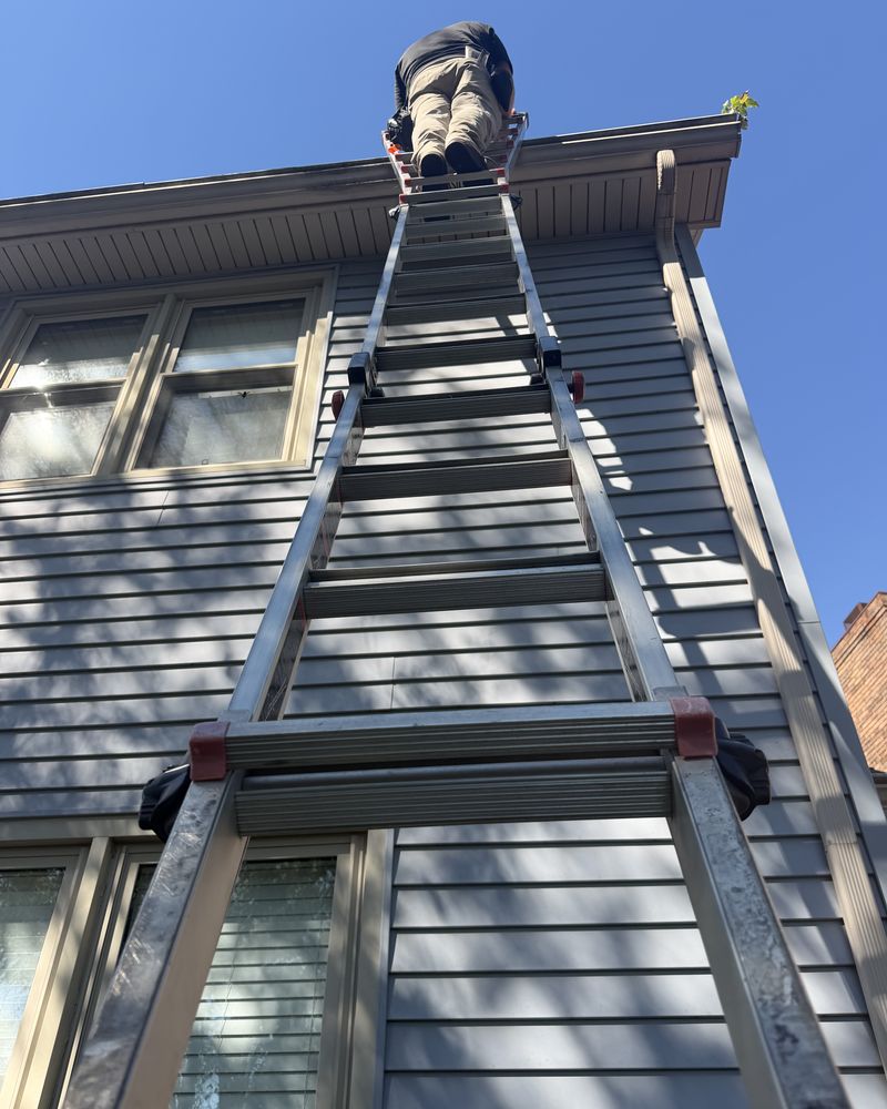 Looking up an extension ladder against blue siding to an adjuster at the edge of the roof