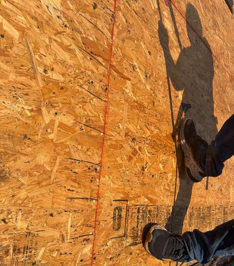 New OSB sheathing on the roof deck during tear-off, with a roofer’s shadow across it