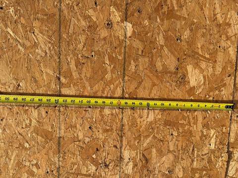 After: new OSB sheathing on the same roof deck during tear-off, with a tape measure across it