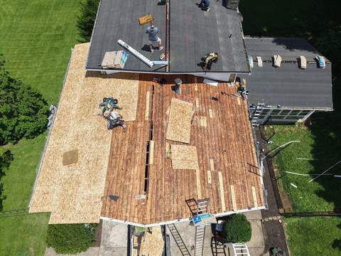 Drone view of tear-off day: part of the roof stripped to the deck while the crew works