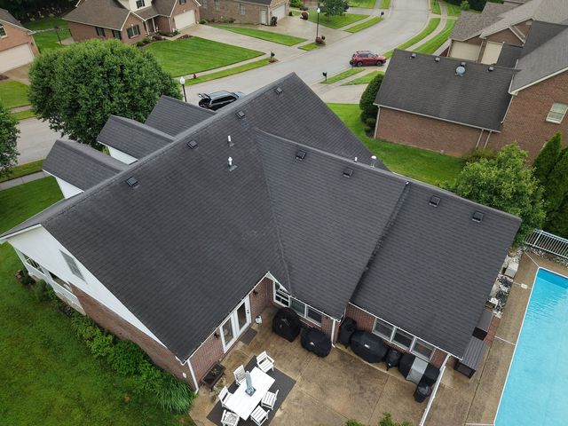 Before: rear drone view of a brick and white-sided home with a worn dark shingle roof above the patio and pool