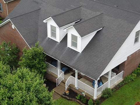 Before: home with two front dormers and a covered porch, seen from above, with its old dark shingle roof