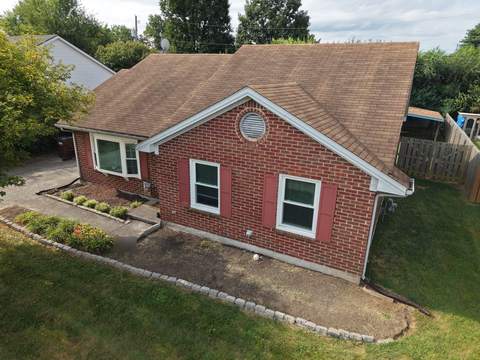 Before: one-story brick ranch with a round gable vent and its worn brown shingle roof
