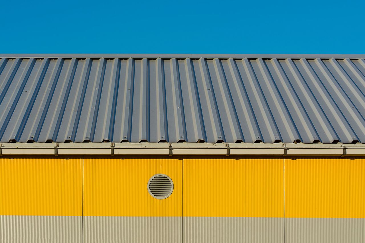 Gray corrugated metal roof on a building with a yellow metal wall, against a blue sky
