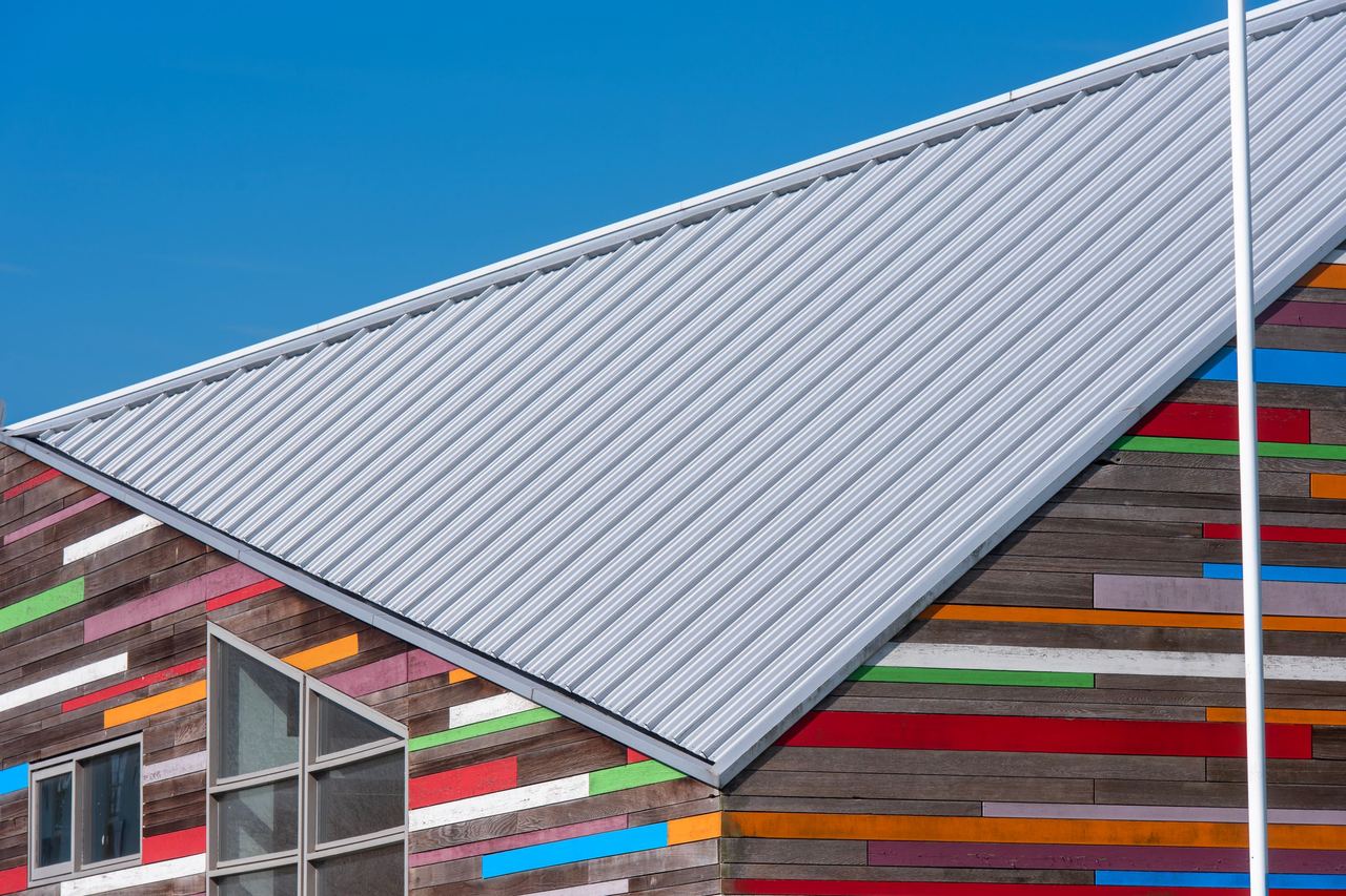 Light gray ribbed metal roof on a modern building with multicolored wood siding